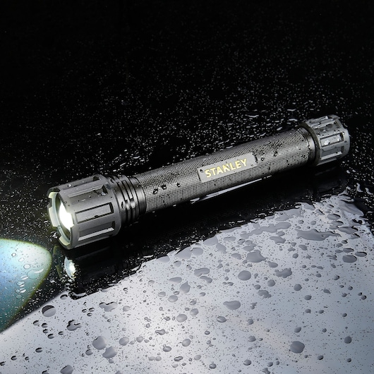 STANLEY SXLS50103E black waterproof flashlight with textured grip, front view, shining on wet surface.
