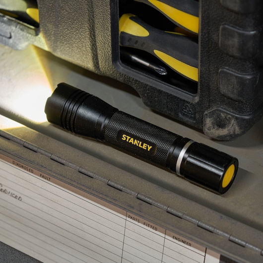 STANLEY SXLS50104E black LED flashlight on workbench with toolbox in background.