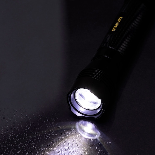 STANLEY SXLS50106E black flashlight shining on wet surface, angled view.
