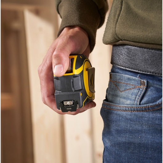 STANLEY XTHT0-33501 tape measure held in hand, close-up, next to jeans pocket, indoor setting.