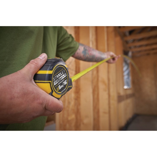 Photo of STANLEY XTHT0-33503 FATMAX tape measure in use, extended inside a wooden construction frame.