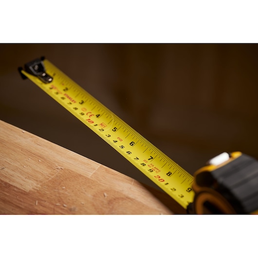 STANLEY XTHT0-33503 tape measure with yellow blade extended on wooden surface, side angle.