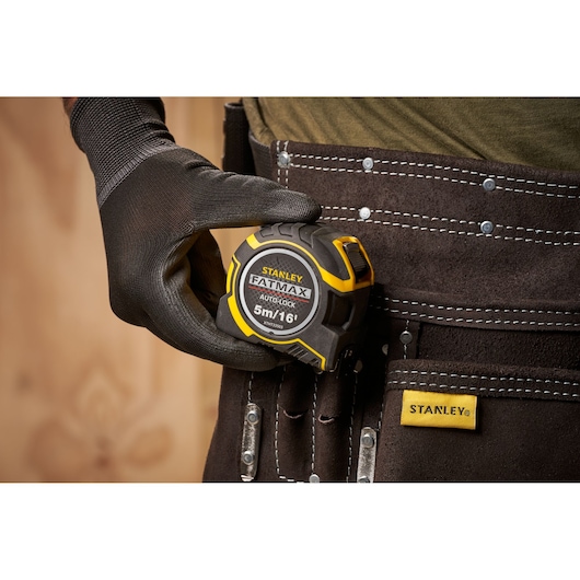 STANLEY XTHT0-33503 tape measure FATMAX 5m, held by gloved hand, tool belt close-up.