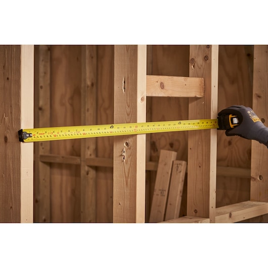 STANLEY XTHT0-33504 tape measure extended against wooden framing, angled view, construction setting.